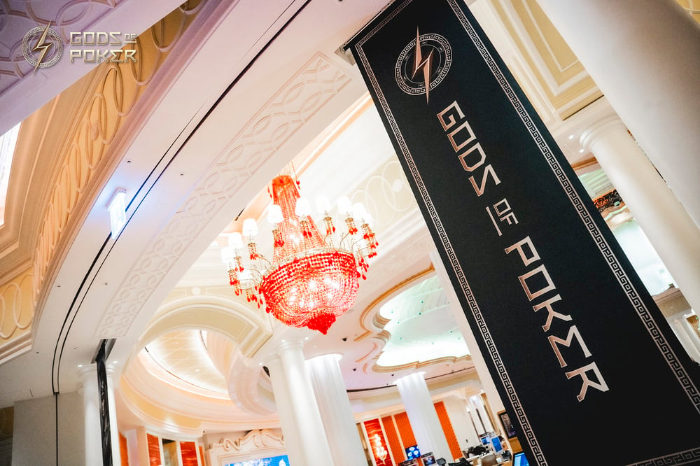 A grand casino interior with a sparkling chandelier and a 'Gods of Poker' banner.
