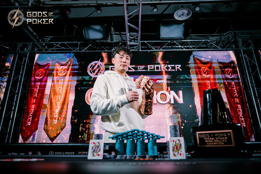 Young man holding a poker trophy and chips, standing before a large screen.