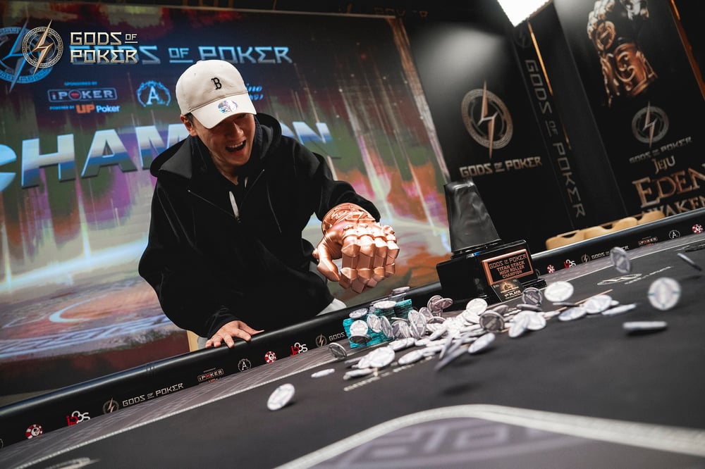 A smiling man in a cap pushes a large pile of poker chips across a table.