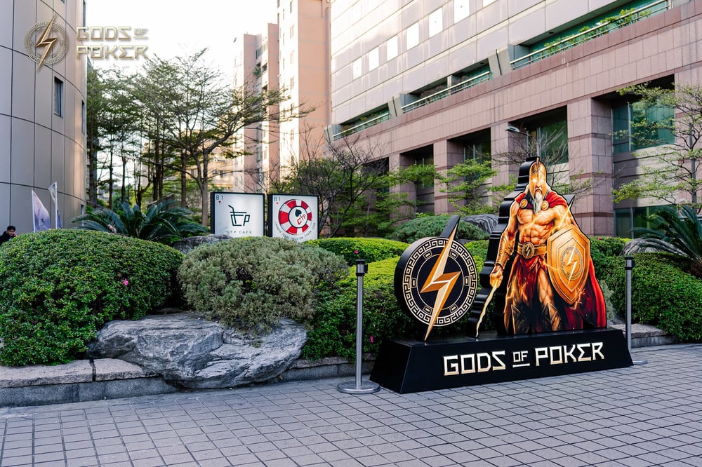 Golden Spartan warrior statue and 'Gods of Poker' sign outside a modern building.